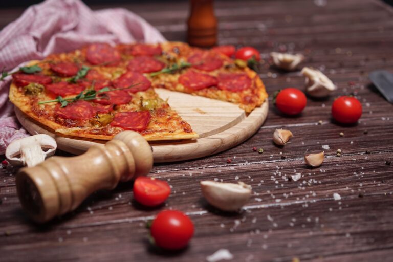 Zbliżenie na pizzę pepperoni na drewnianej desce z pomidorkami koktajlowymi i ząbkami czosnku na rustykalnym stole